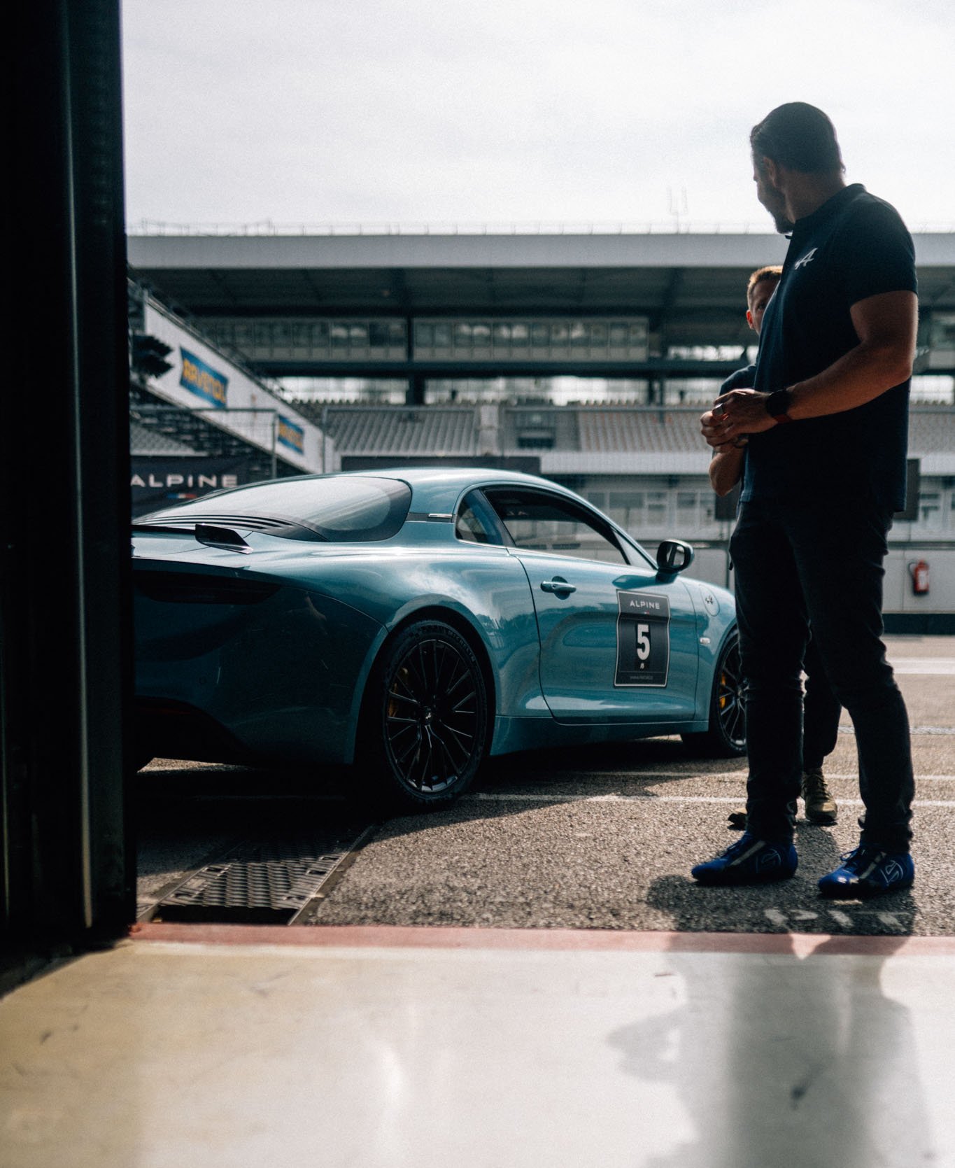 [Translate to Französisch:] Alpine A110 die in der Boxengasse steht und aus der Pitbox fotografiert wurde. Ein Fahrer schaut sich sie an.