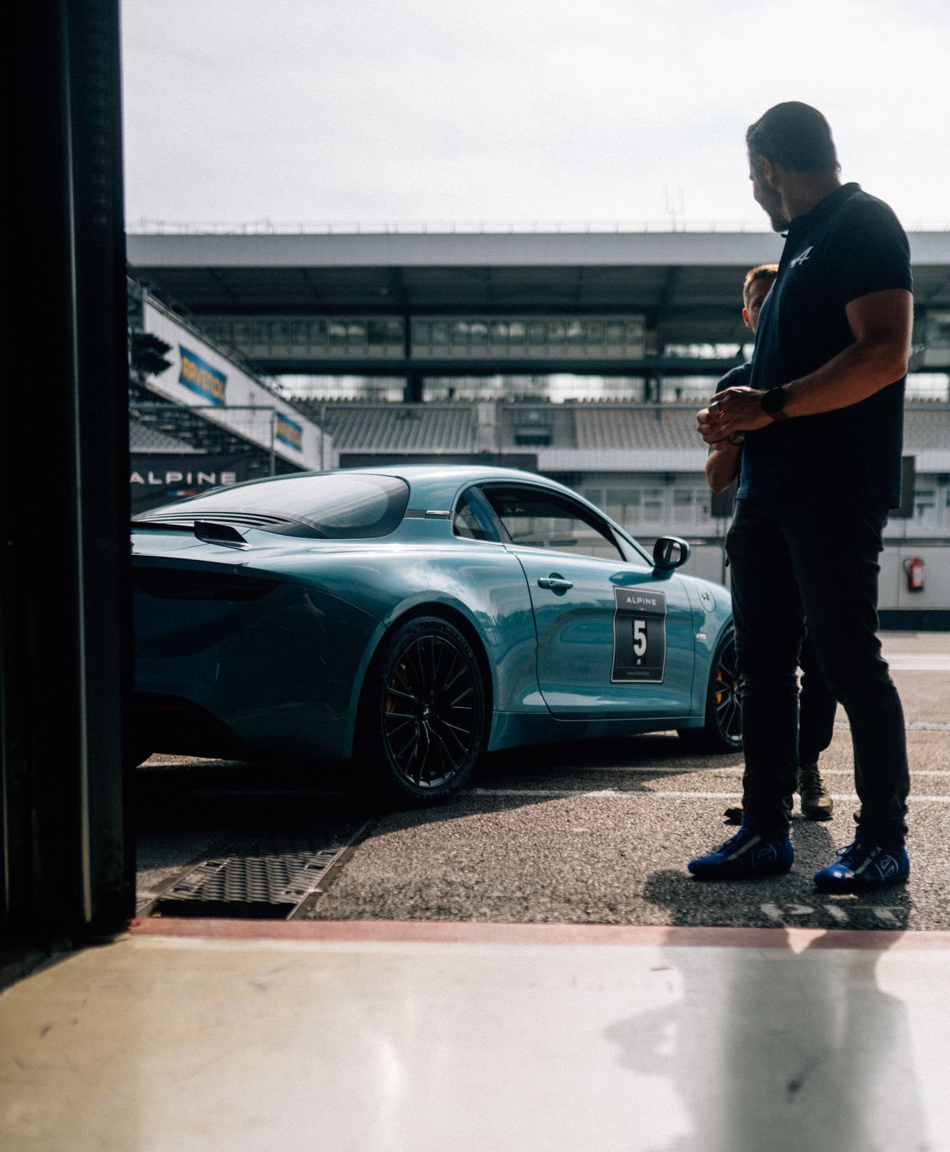 Alpine A110 die in der Boxengasse steht und aus der Pitbox fotografiert wurde. Ein Fahrer schaut sich sie an.