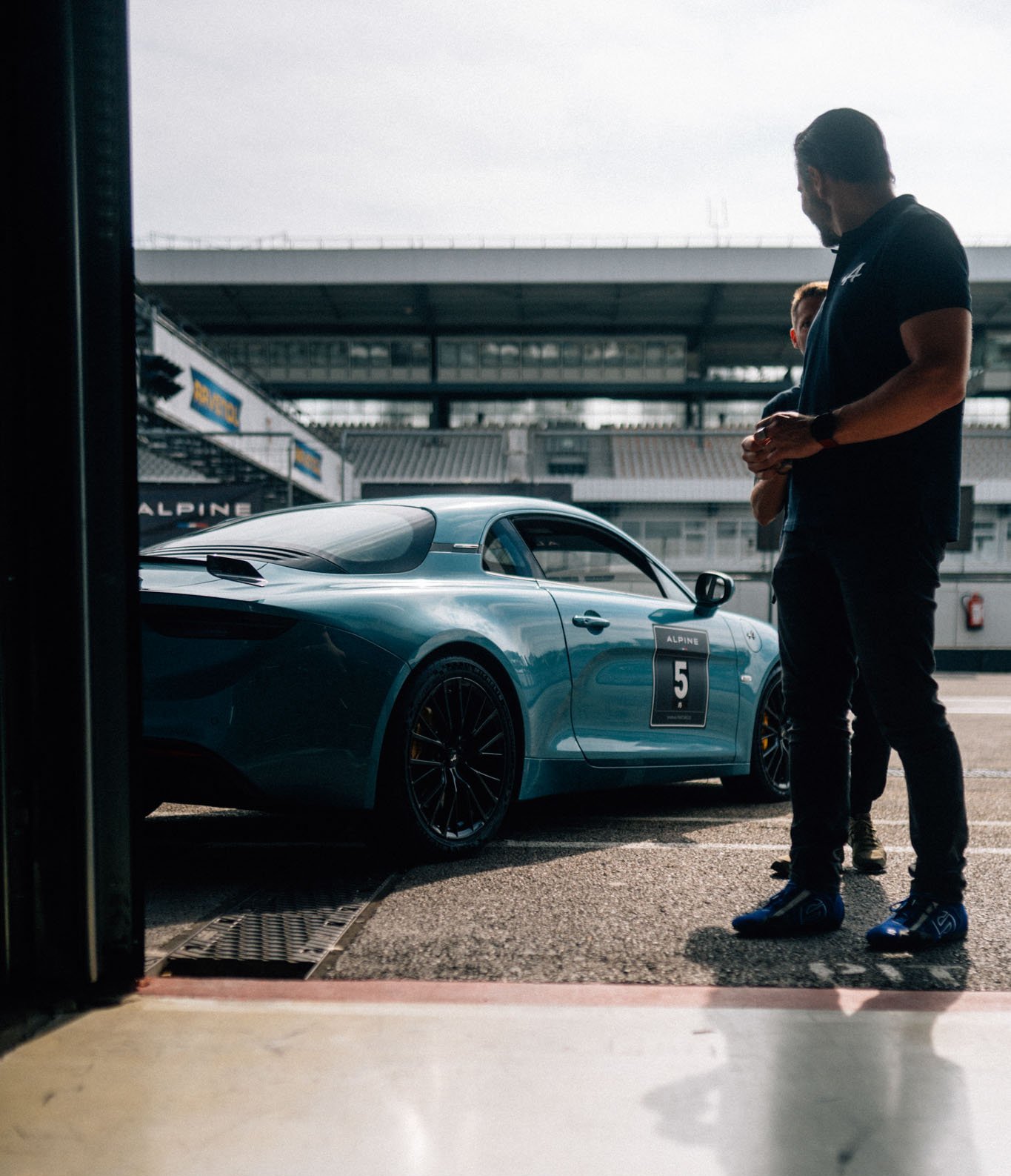 [Translate to Englisch:] Alpine A110 die in der Boxengasse steht und aus der Pitbox fotografiert wurde. Ein Fahrer schaut sich sie an.